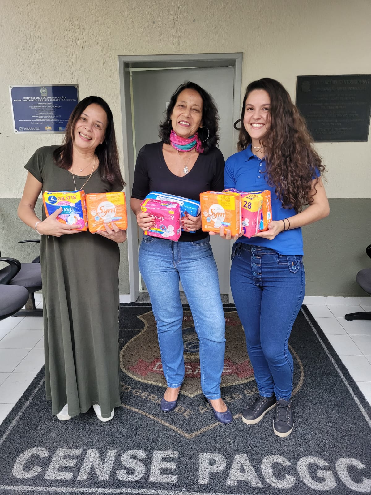 Profissionais segurando pacotes de absorventes na entrada do Cense PAGC