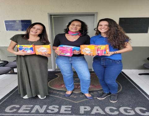 Profissionais segurando pacotes de absorventes na entrada do Cense PAGC