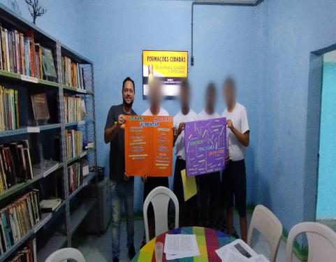 Jovens na Biblioteca do Cense, segurando cartaz 