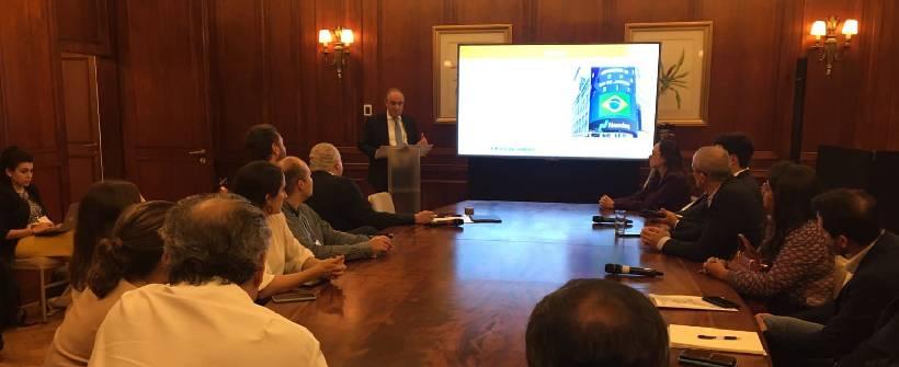 Em uma sala com pessoas em volta de uma mesa, Nelson Rocha, em pé e em frente a telão, apresenta projeto da Seplag