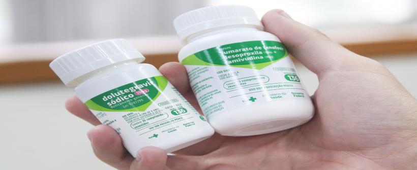 Uma mão direita branca segura dois frascos de medicamentos, são da Profilaxia Pós-Exposição