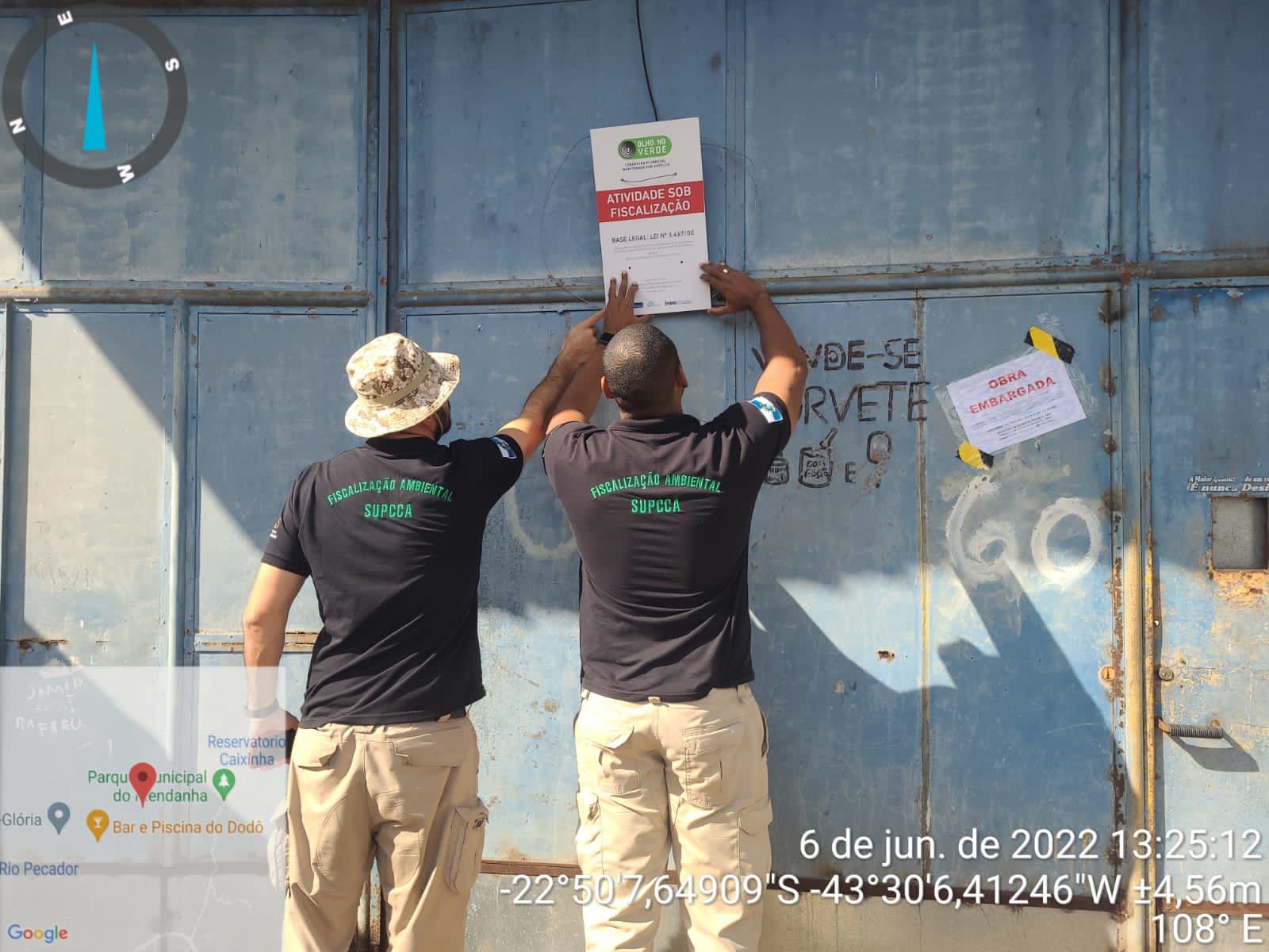 Dois agentes da fiscalização ambiental colando um cartaz no portão de obra embargada