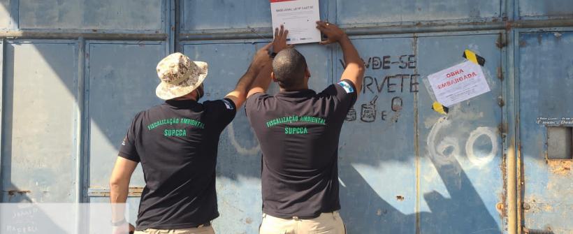 Dois agentes da fiscalização ambiental colando um cartaz no portão de obra embargada