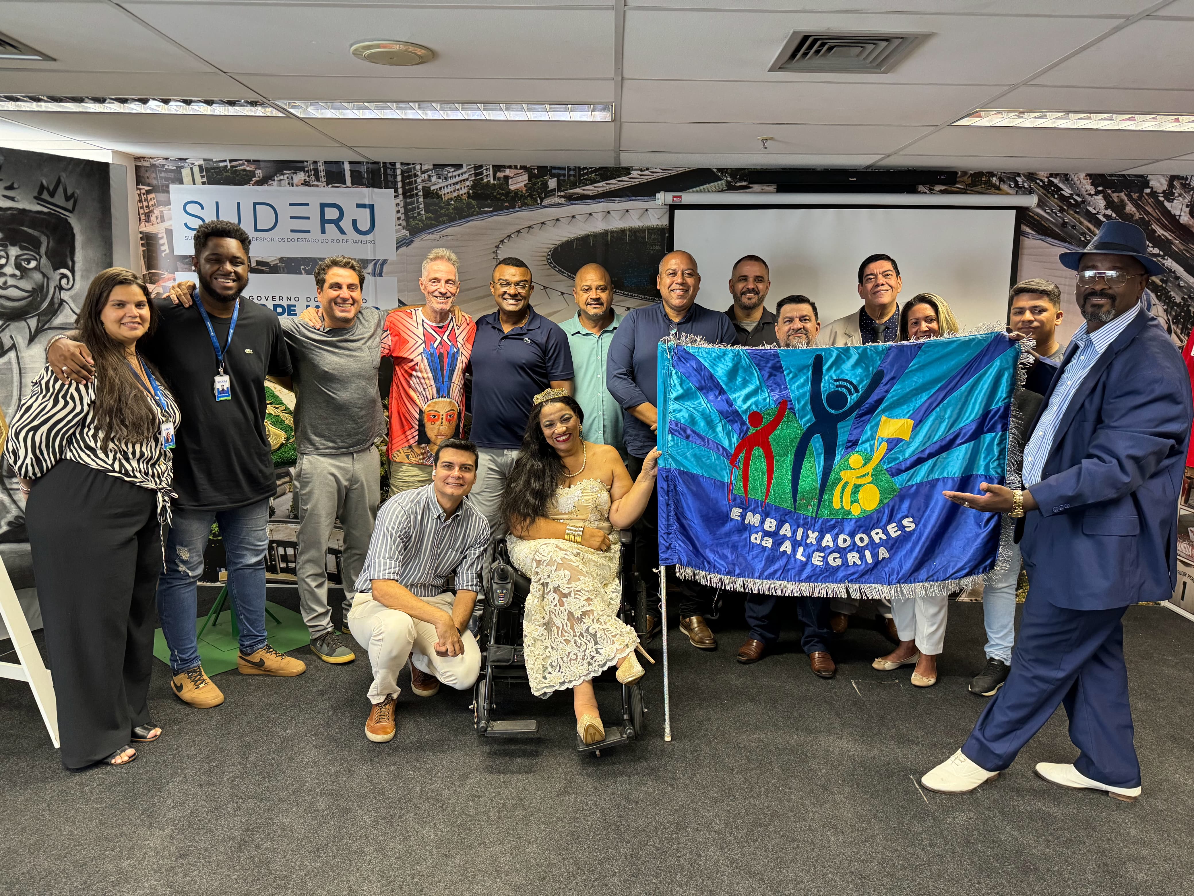 Um grupo de pessoas sorrindo para foto com uma bandeira em destaque
