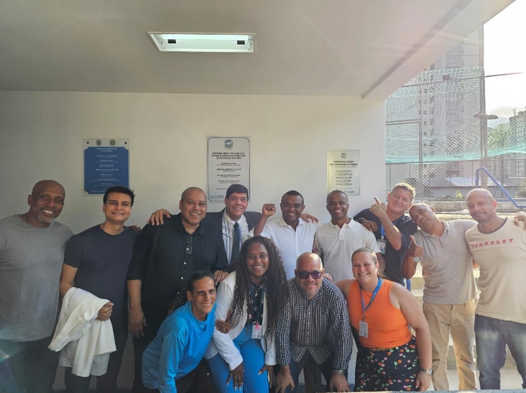 Grupo de pessoas sorrindo ao lado de uma placa na parede.