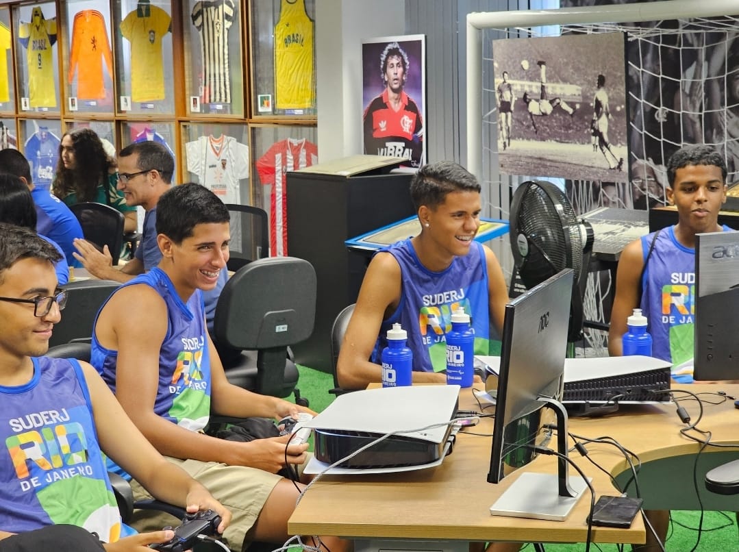 Quatro jovens com camisas azuis, sorrindo ao jogar vídeo game